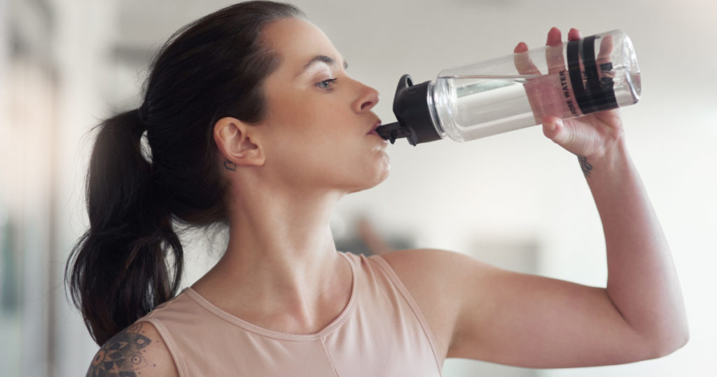 Stay active and stay hydrated. a young athlete drink water while at the gym.
