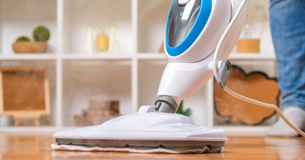 A man washes the floors with a steam mop. Floor treatment with hot steam. Hygienic control of cleanliness.