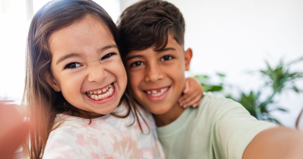Hispanic little siblings taking a selfie at home - preschool girl and elementary school boy happy siblings social media