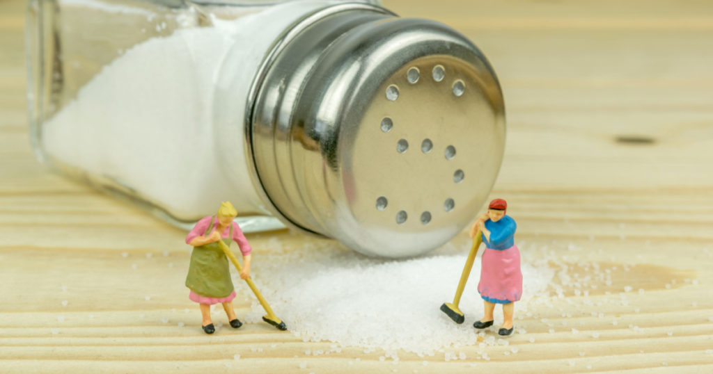 Miniature toy housewives figures cleaning up spilled salt on wooden table