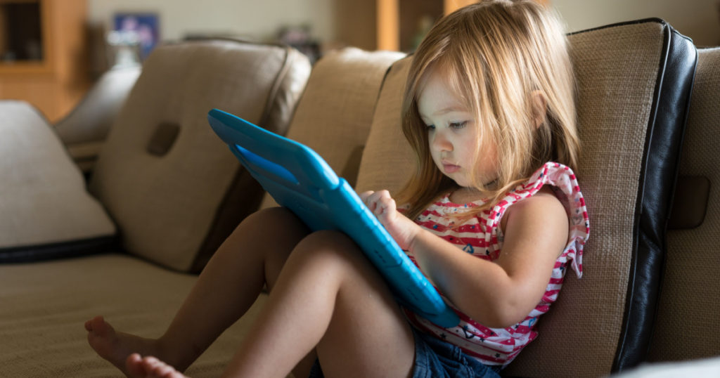 Young girl sitting at home on settee and using a child's tablet touch screen computer
