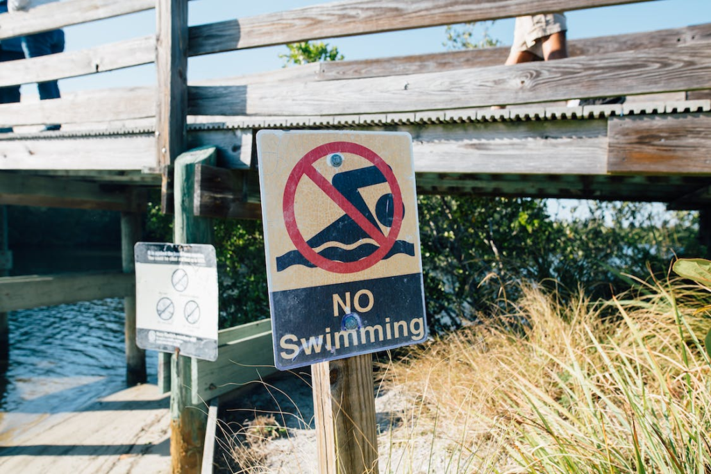 No swimming sign placed at lakeside near wooden quay
