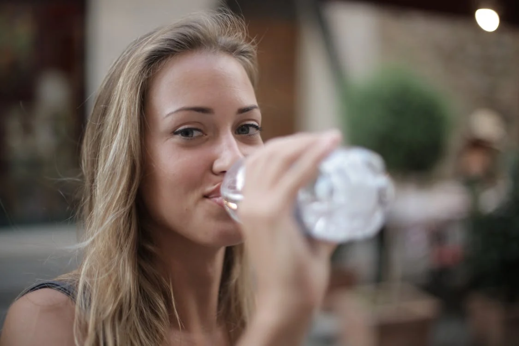 Selective Focus Photo of Smiling Woman Drinking Water from a Plastic Bottle
