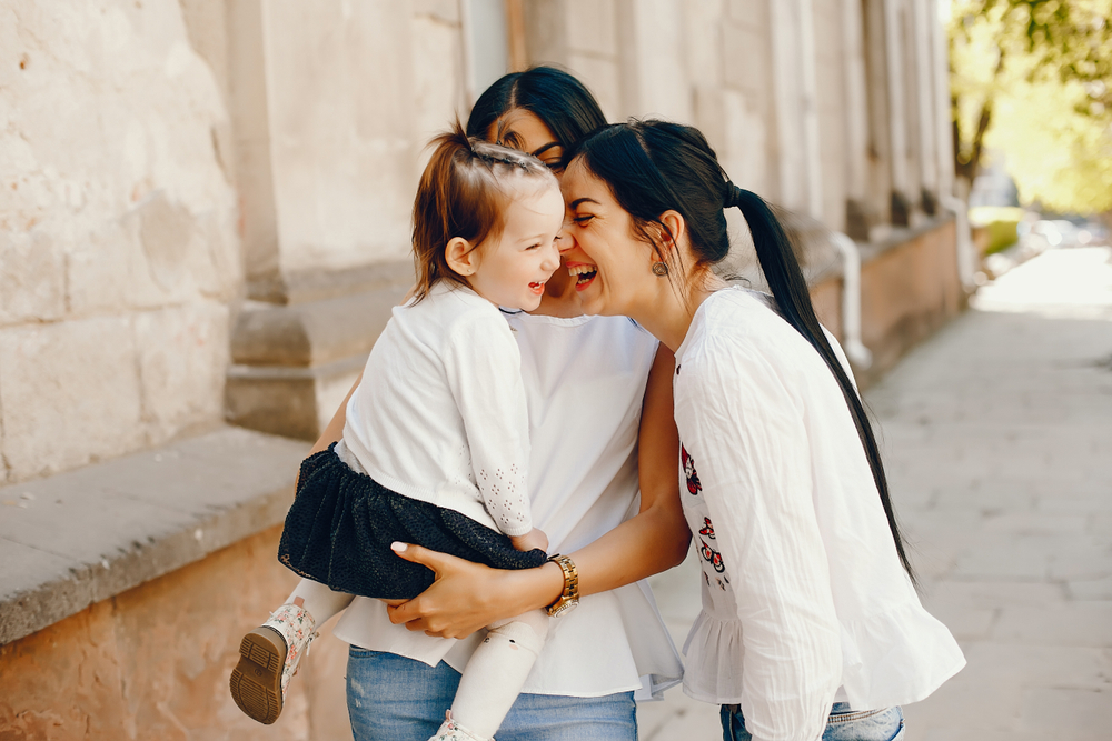 Mother with little daughter. Aunt with her niece walk in a summer city. Three girls have fun in a town. Little girl with her two sisters