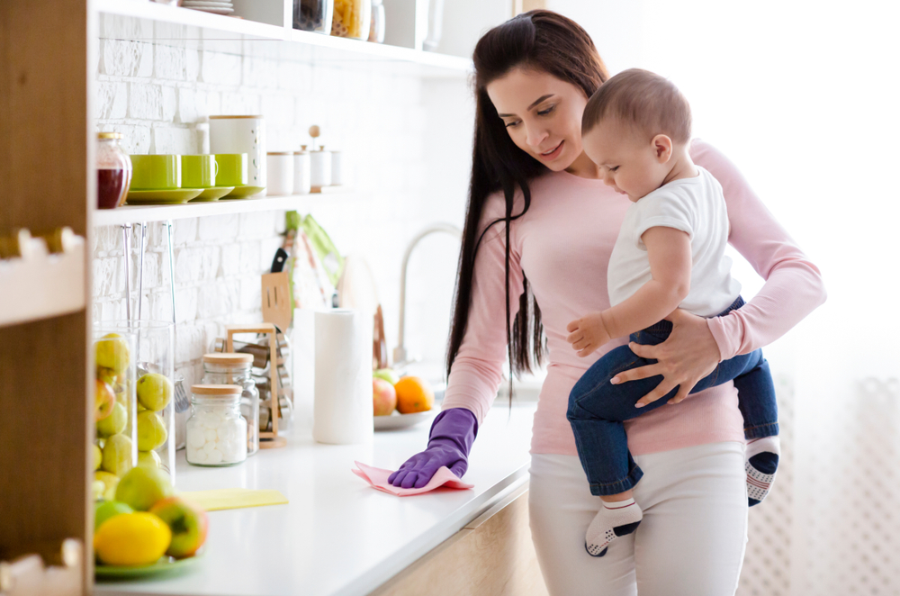 Domestic chores at maternity leave. Young mother with baby boy cleaning kitchen at home, free space
