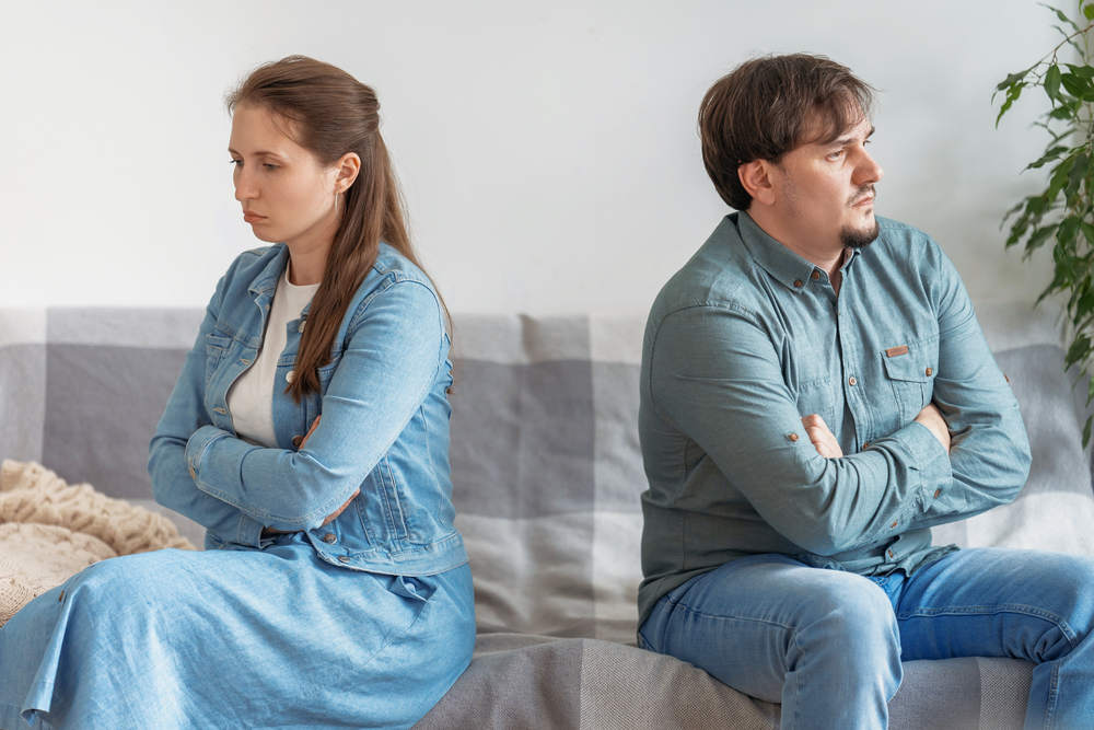 Husband and wife, feeling upset after an argument, sit back to back, facing away from each other. frustrated young girl and boyfriend avoid talking, couple tired bad relationship, sitting on couch