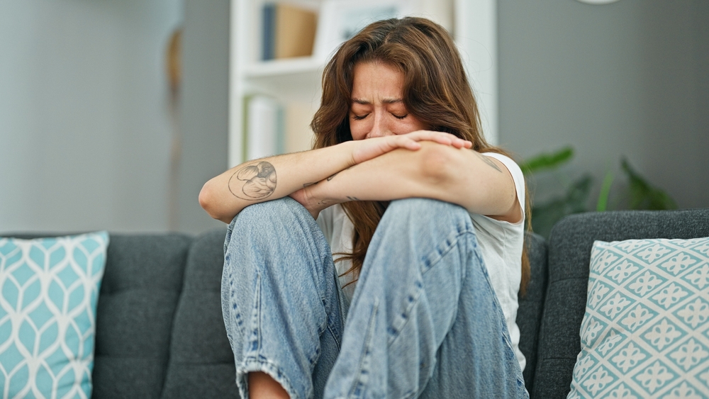 Young beautiful hispanic woman sitting on the sofa crying at home
