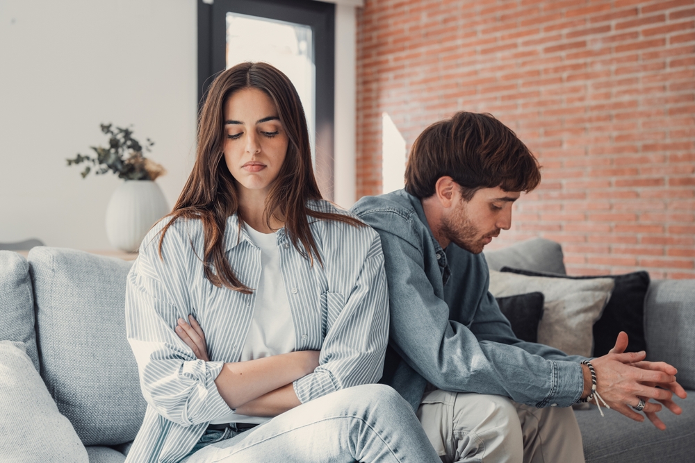 Beautiful lady is depressed, sitting on the couch talking to man, having a dispute with husband or boyfriend, looking desperate and hopeless, having unresolved problem or question