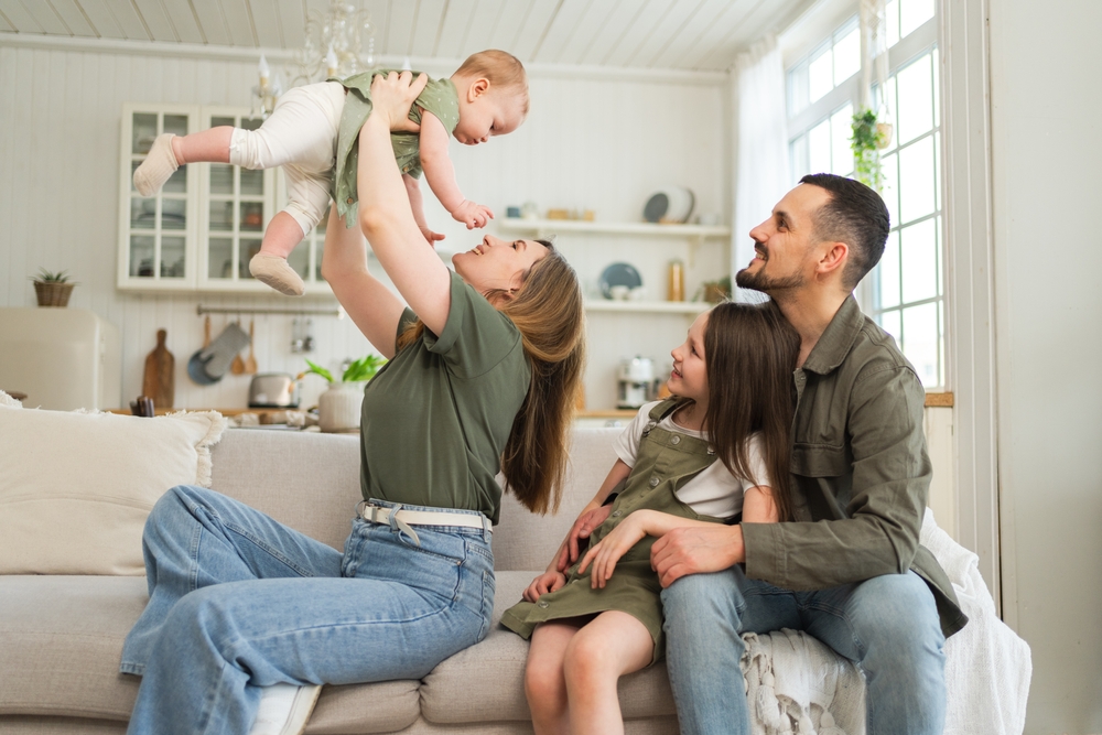 Happy family at home. Mother father two children daughters relaxing on sofa indoor. Mom dad parents baby girls kids relax playing having fun together. Family smiling laughing enjoying tender moment