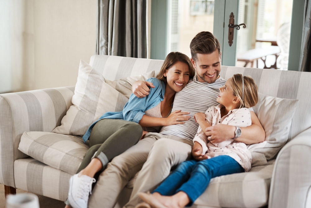 Parents, girl and happy on sofa with hug, conversation or funny story for bonding, care and love in lounge. Father, mother and daughter with embrace, laugh and memory with connection in family home