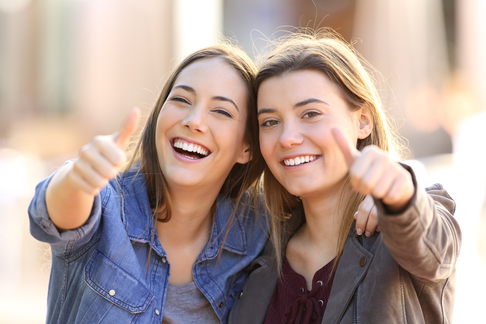 Front view portrait of two funny friends with thumbs up and looking to the camera in the street