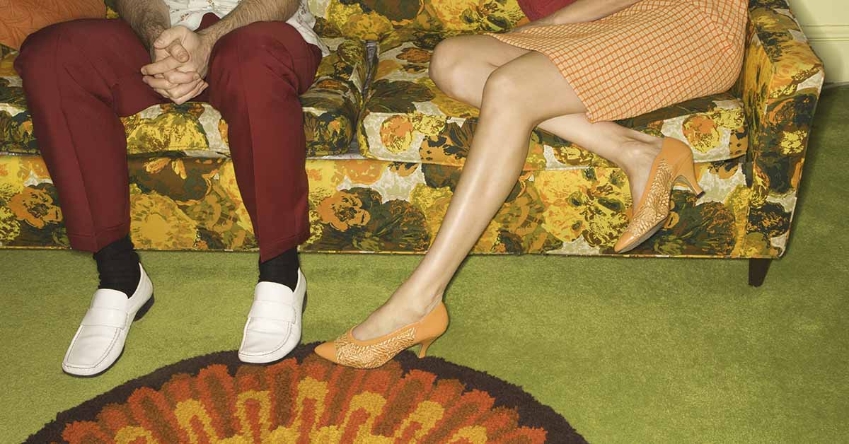 Two people sitting on a colorful patterned couch. 1970s concept