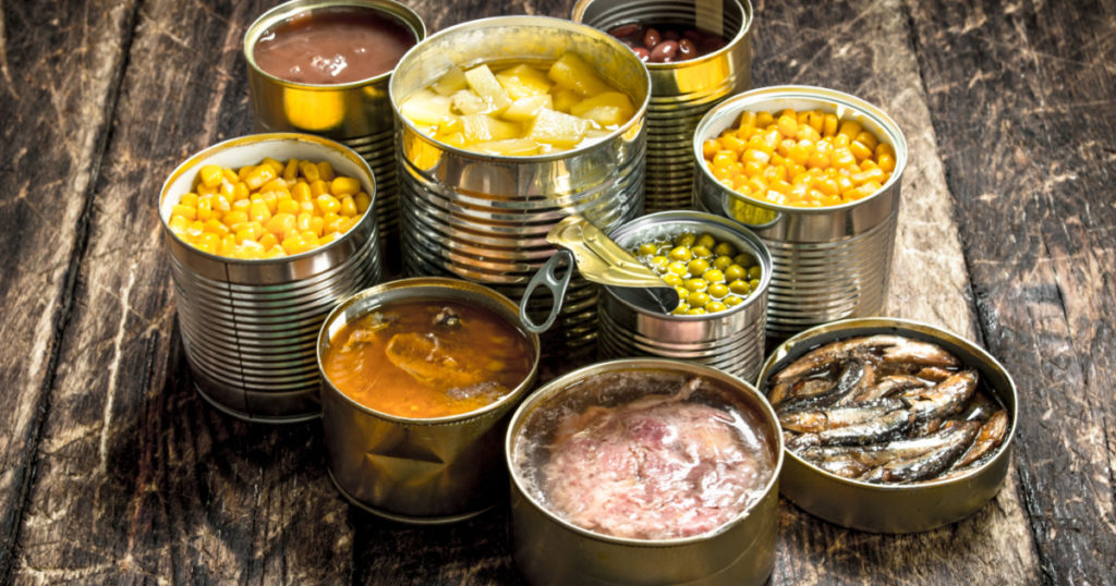 Various canned vegetables, meat, fish and fruits in tin cans. On a wooden background.
