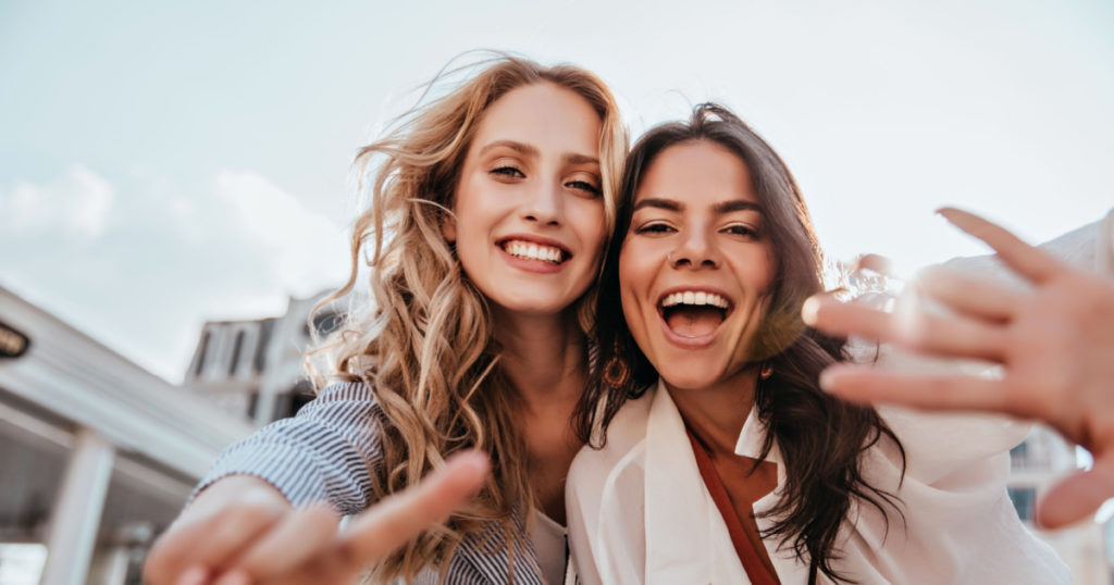 Lovable caucasian girls expressing positive emotions to camera. Outdoor photo of refined sisters posing on sky background.