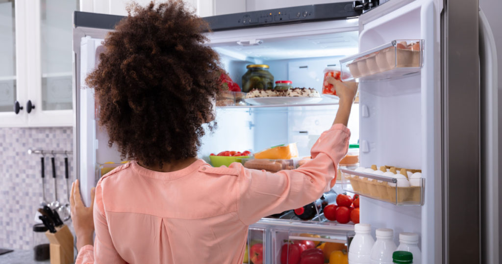Rear View Of A Young Woman Taking Food To Eat From Refrigerator
