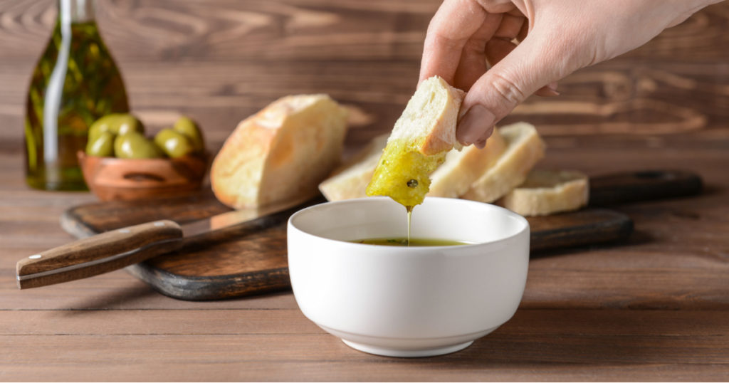 Woman dipping fresh bread into tasty olive oil in bowl
