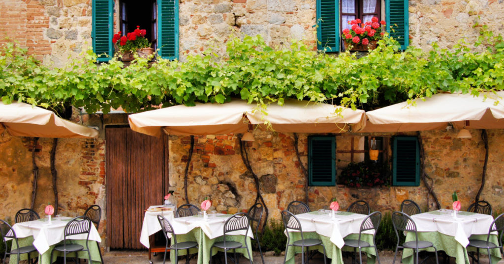 Cafe tables and chairs outside a quaint stone building in Tuscany, Italy