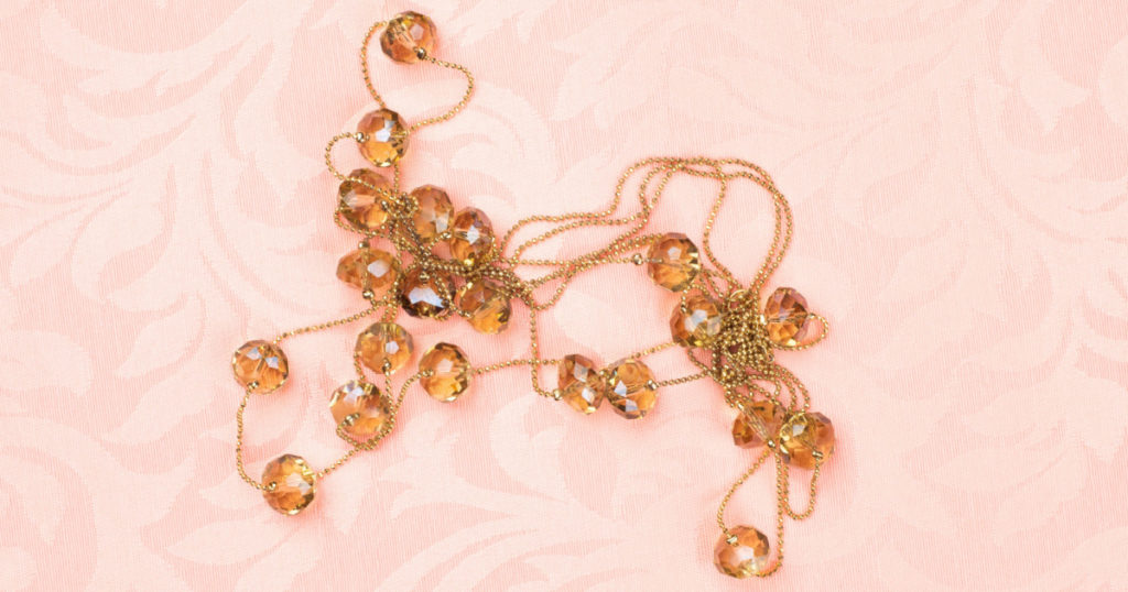 A Tangled, Gold Tone Necklace on a Pink Damask Fabric Background with copy space. It's horizontal but works as Vertical
