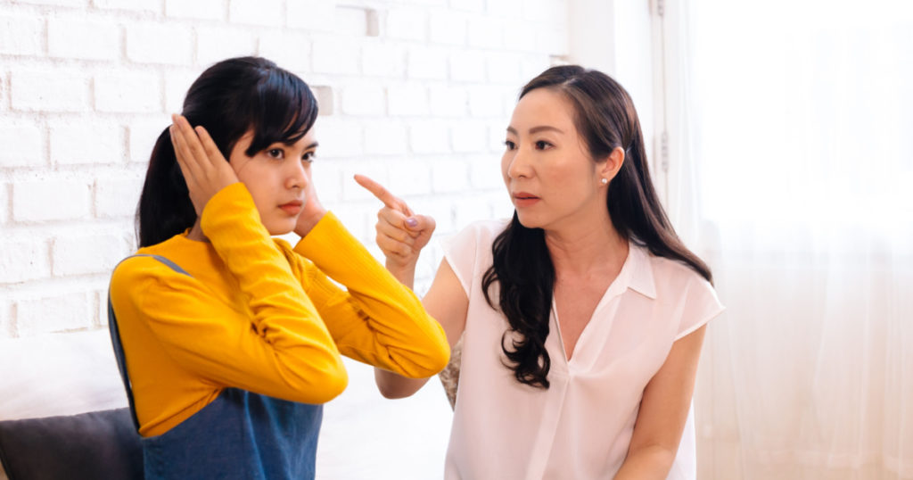Argument between annoyed Asian teenage daughter and upset middle aged mother. The child covering ears while mum pointing finger at. Bad, unhealthy, toxic family relationship concept