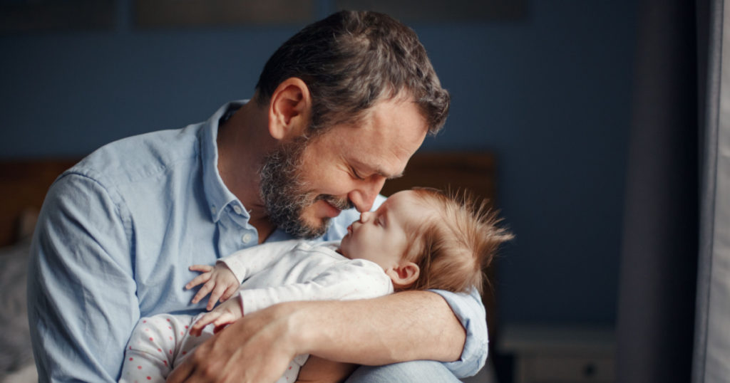 Middle age Caucasian father kissing sleeping newborn baby girl. Parent holding rocking child daughter son in hands. Authentic lifestyle parenting fatherhood moment. Single dad family home life.
