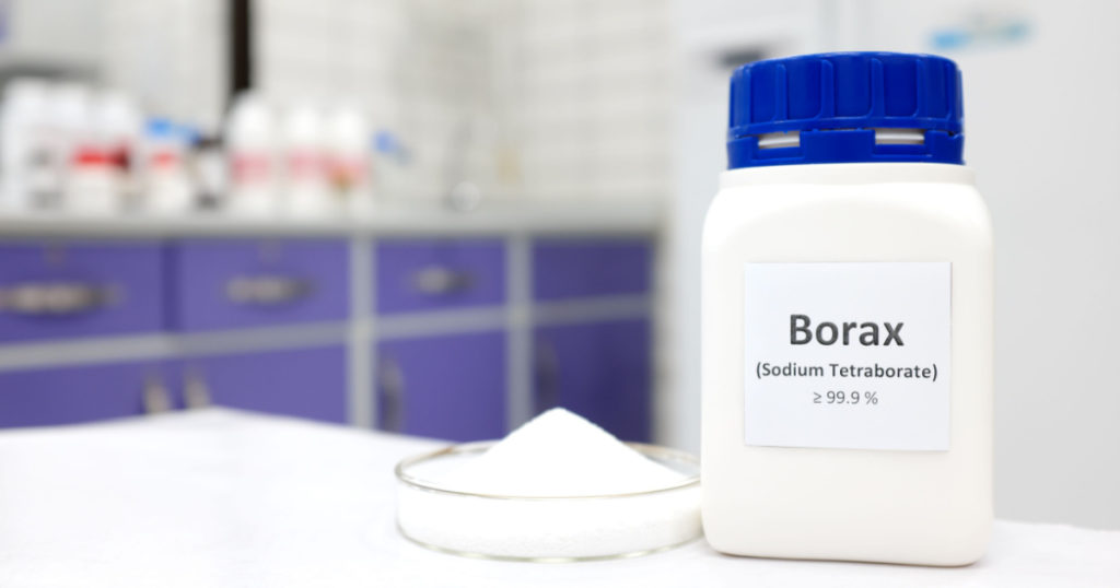 Selective focus of a bottle of borax chemical compound or sodium tetraborate beside a petri dish with solid powder substance. White Chemistry laboratory background with copy space.