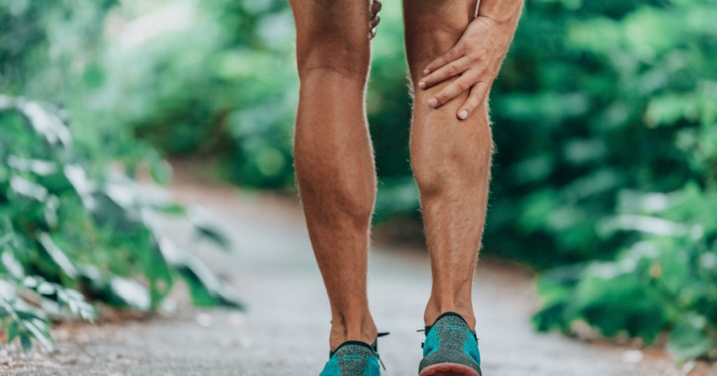 Runner leg injury painful leg. Man massaging sore calf muscles during running training outdoor from pain.