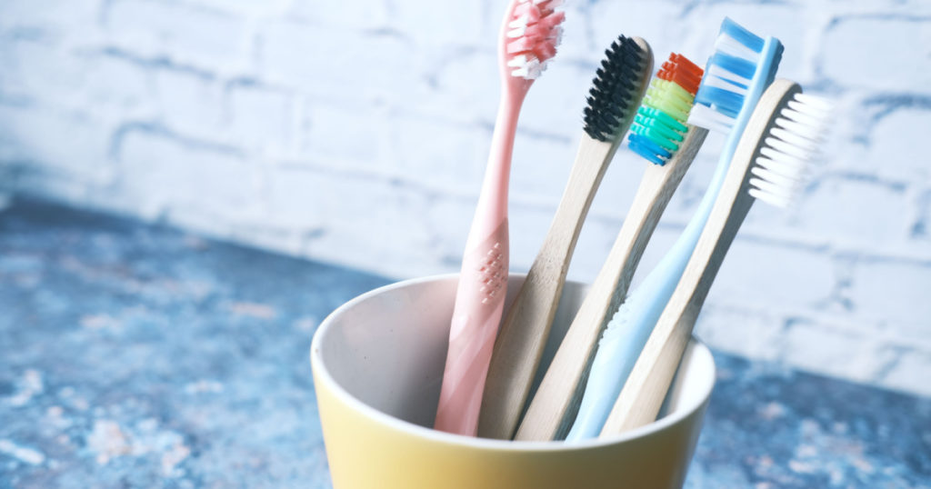colorful toothbrushes in white mug against a wall