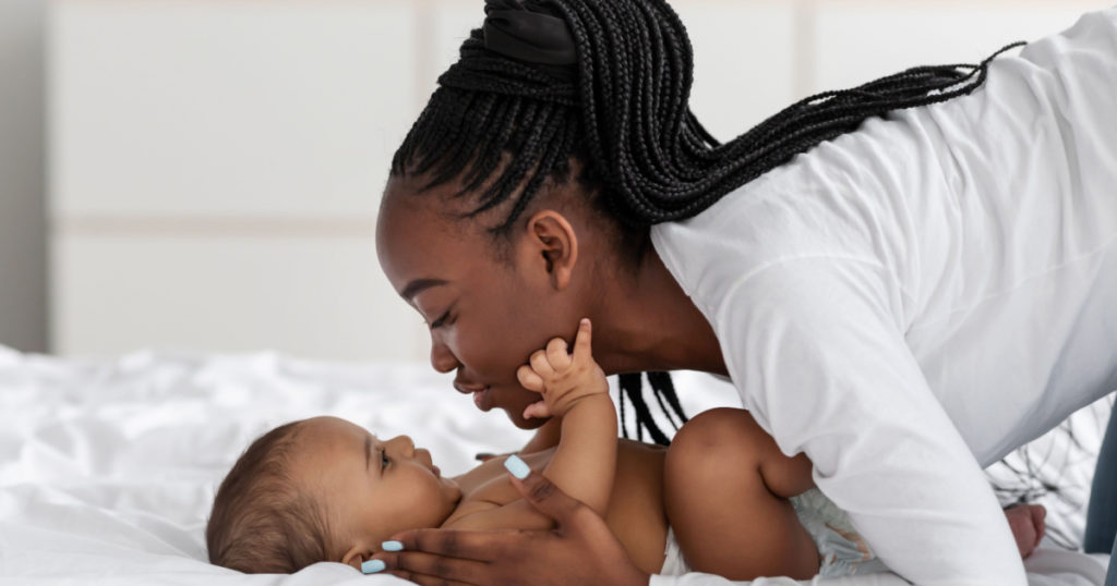 Black mom playing in bed with her infant, kissing baby