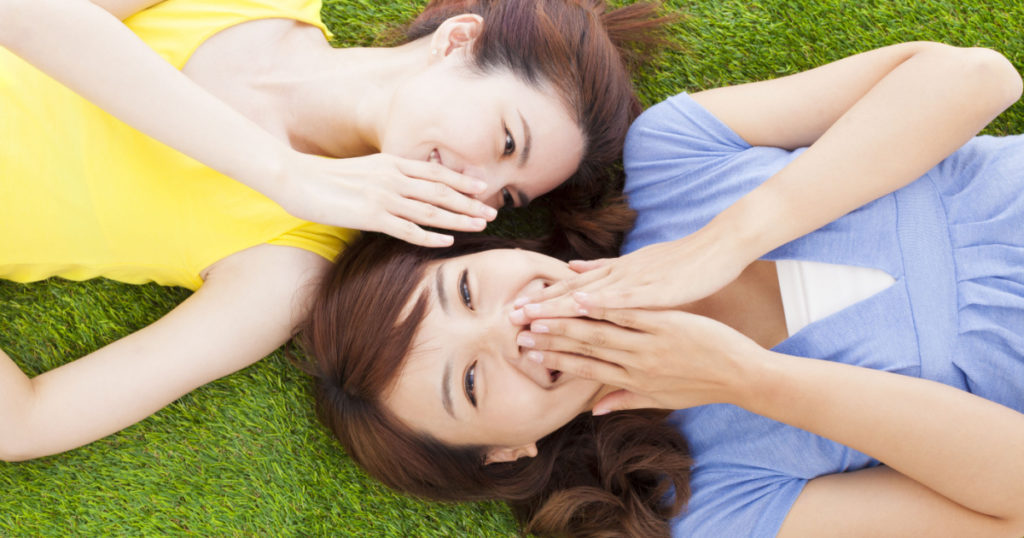two asian sisters whispering gossip on the grass