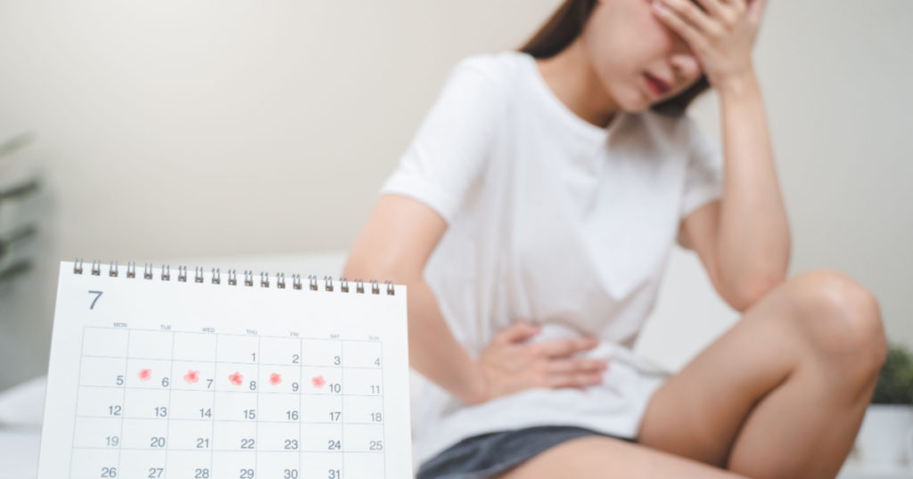 Monthly menstruation symptom period concept. Close up calendar marking on menstruation period day and woman have stomach pain as background.