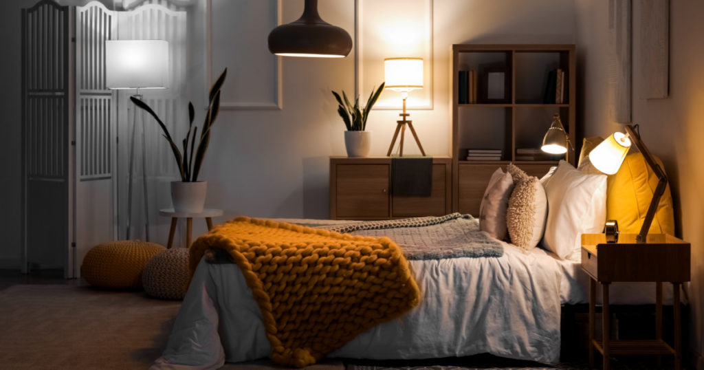 Interior of bedroom with knitted plaid on bed and glowing lamps at night
