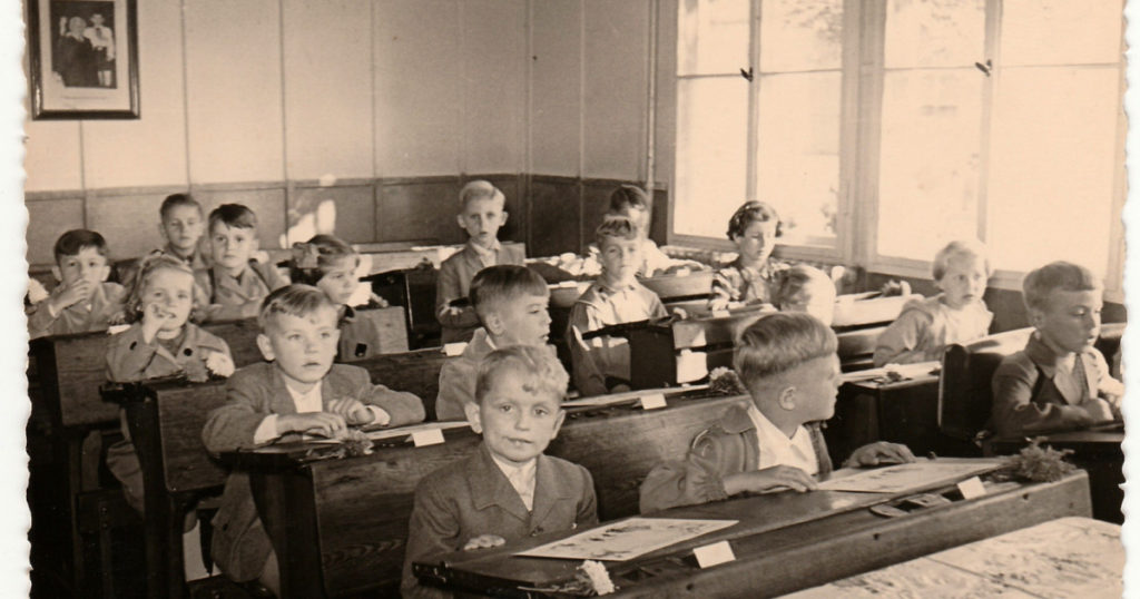 THE CZECHOSLOVAK SOCIALIST REPUBLIC - CIRCA 1950s: Retro photo shows pupils sit at the wooden school desks in the classroom. Vintage photo of group of schoolmates in their classroom.