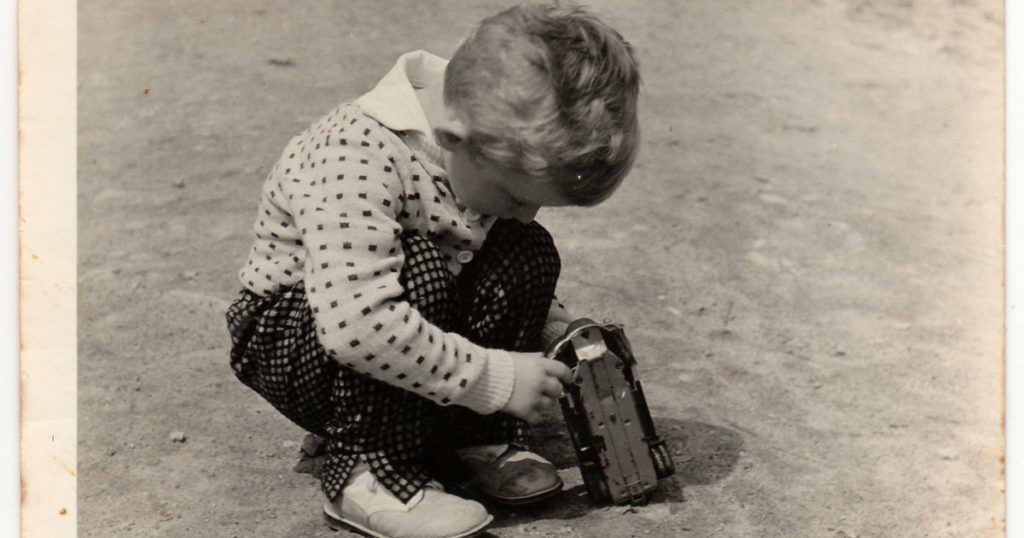 THE CZECHOSLOVAK SOCIALIST REPUBLIC - CIRCA 1960s: Vintage photo shows boy plays with toy car outdoors. A little boy outside plays with a toy automobile. Antique black and white photography. The 60s.