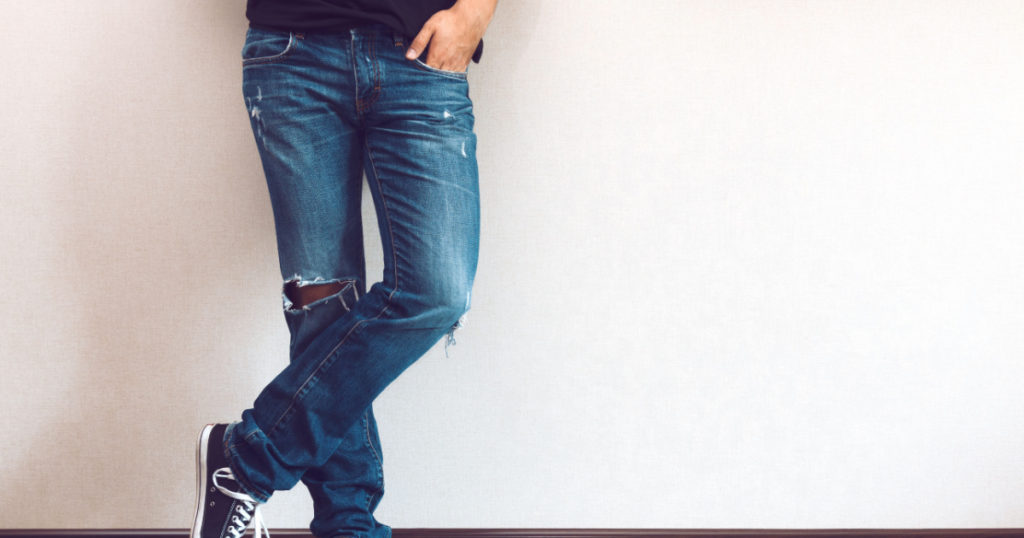 Young fashion man's legs in jeans and sneakers on wooden floor