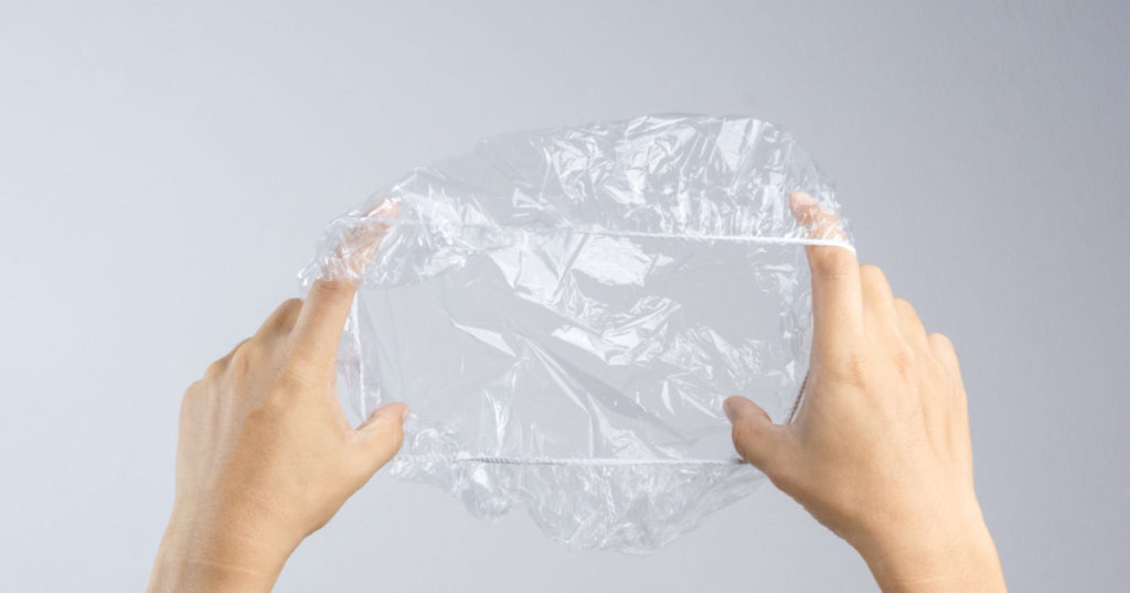 Hand holding disposable transparent plastic shower cap on white background