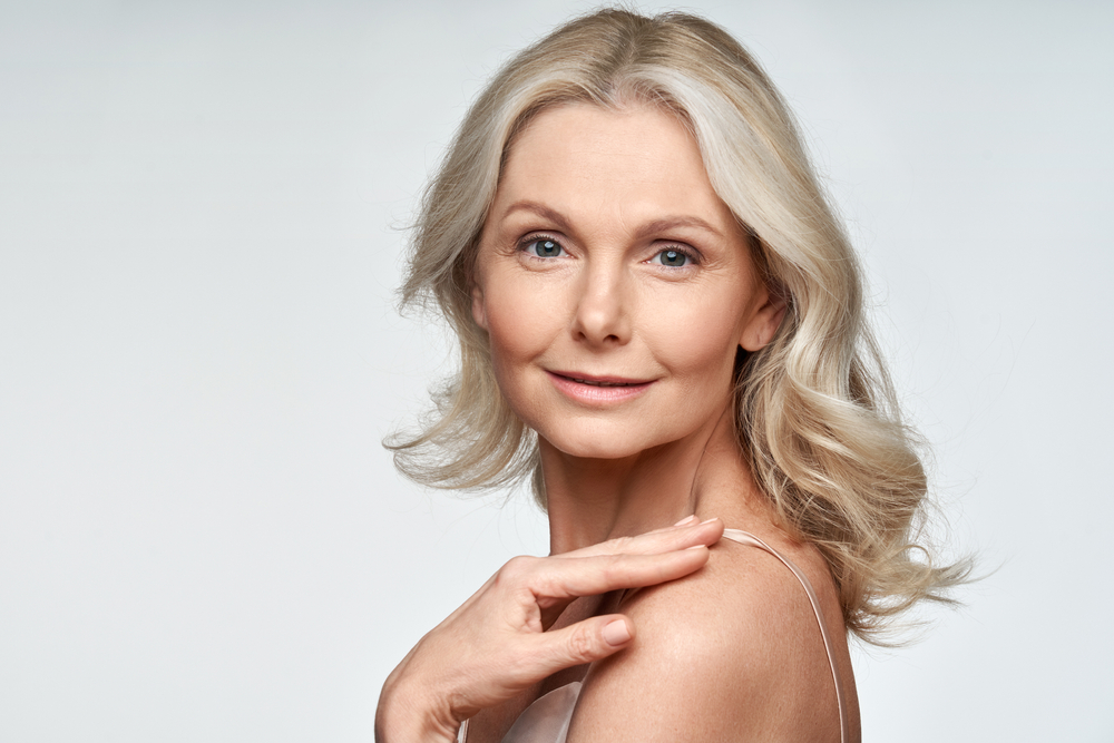 Attractive gorgeous mature older woman looking at camera isolated on white background advertising skincare spa treatment. Mid age tightening face skin care rejuvenation cosmetics concept. Portrait