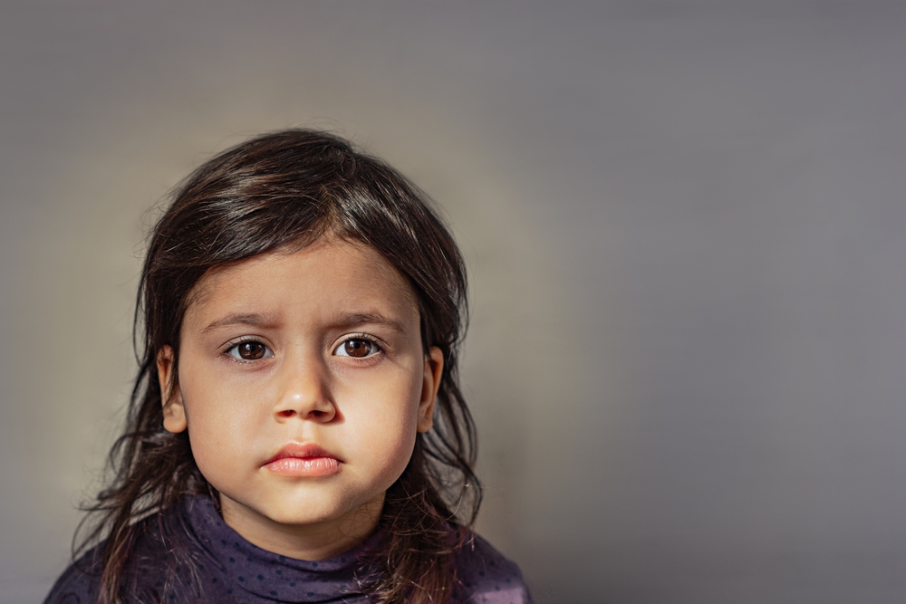 Close-up portrait of a charming 3 year old girl. The child looks sadly at the camera. girl with dark eyes and hair