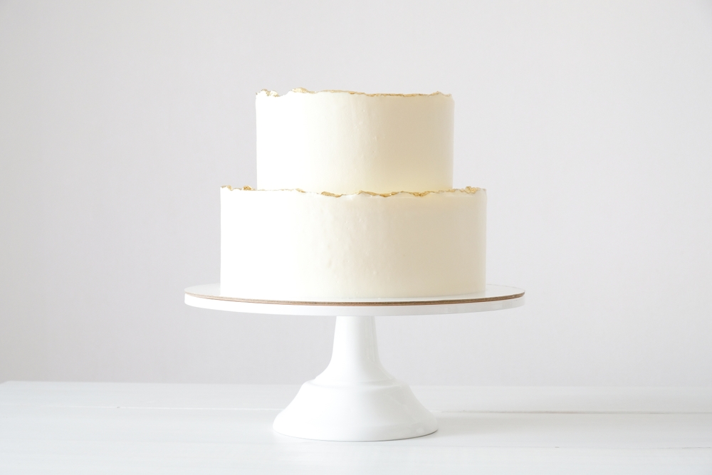 Cake with white cream, decorated with gold confectionery sprinkles on a white background. Two-tiered white wedding cake.