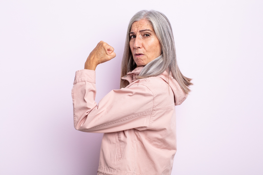 middle age gray hair woman feeling happy, satisfied and powerful, flexing fit and muscular biceps, looking strong after the gym