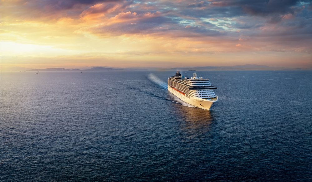 Panoramic aerial view of a cruise ship traveling over the ocean during golden summer sunset time with copy space
