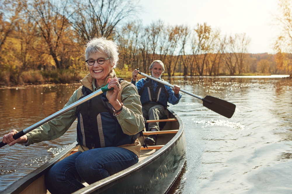 Lake, rowing and kayak with old couple, nature and retirement with happiness, relax and vacation. Outdoor, river and mature man with senior woman, freedom and trust with holiday and weekend break