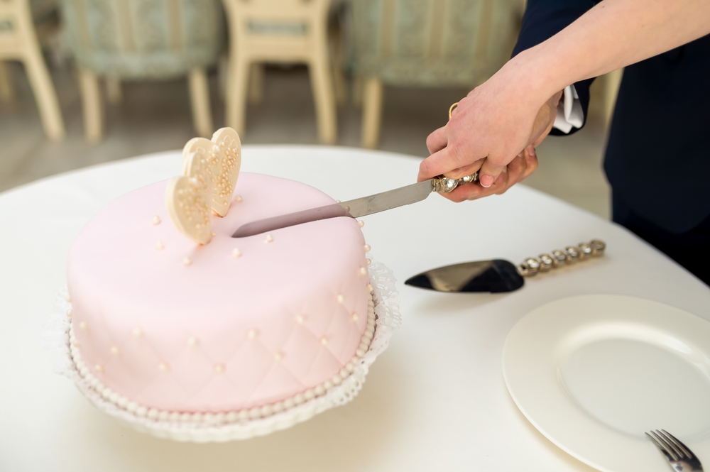 A couple cuts their wedding cake with a silver knife, a tradition symbolizing their new life together.