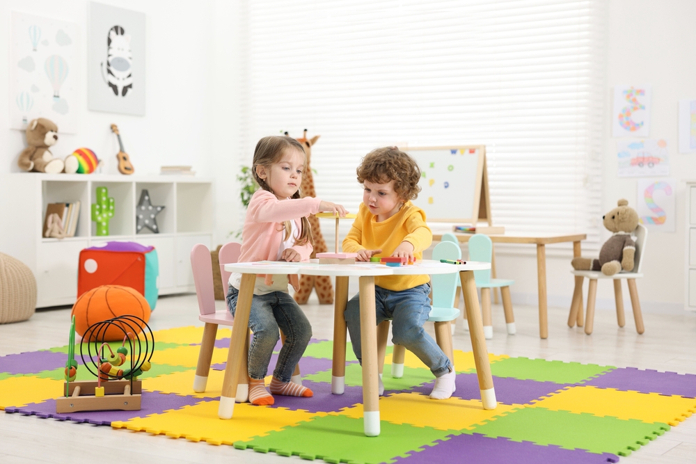 Cute little children playing with colorful toy pyramid at white table in kindergarten
