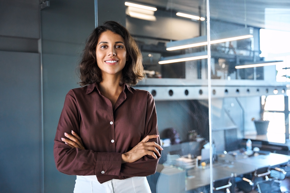 Portrait of beautiful successful hispanic young business woman with crossed arms smiling confident at camera. Latin or eastern middle age female ceo leader businesswoman standing in office. Copy space