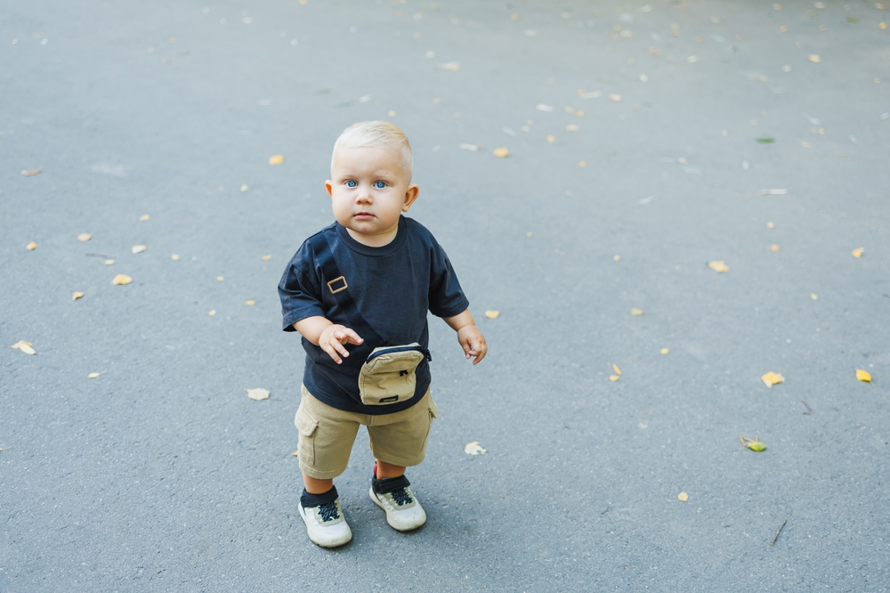A fair-haired toddler walks down the street and plays. A child walking on the street.