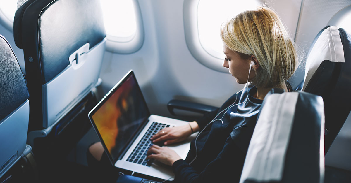 woman on a commerical fight. She is sitting in her seat wearing headphones and using a laptop.