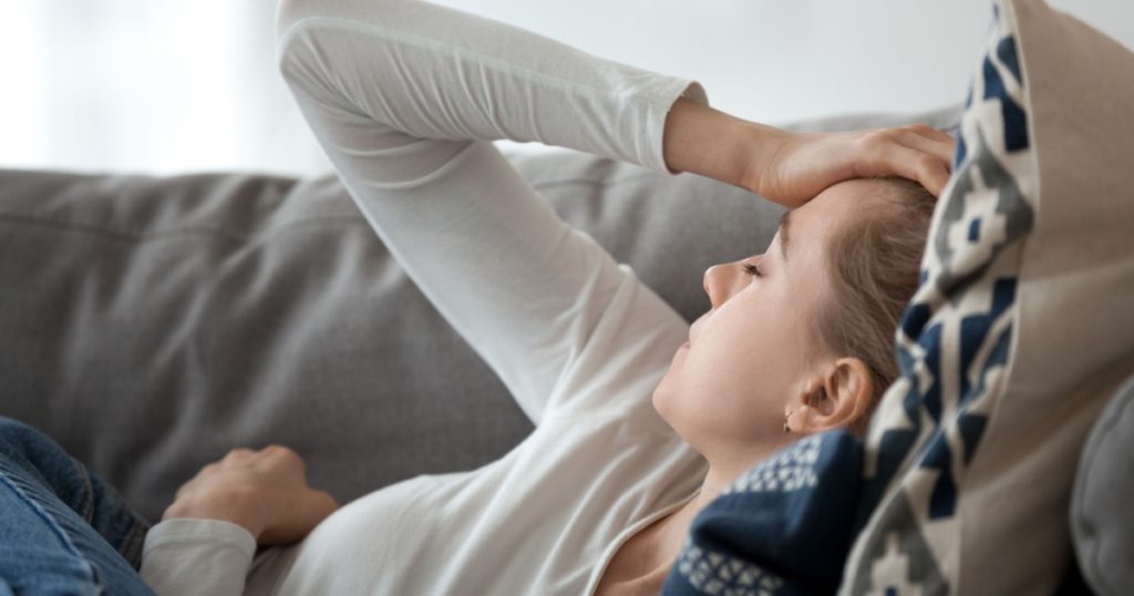 Upset depressed young woman lying on couch feeling strong headache
