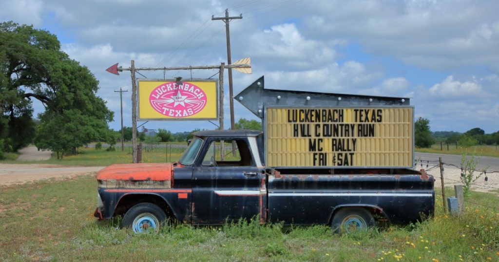 An old truck with a sign in its bed providing directions and a listing events in Luckenbach - Luckenbach, Texas, USA - May 5, 2019