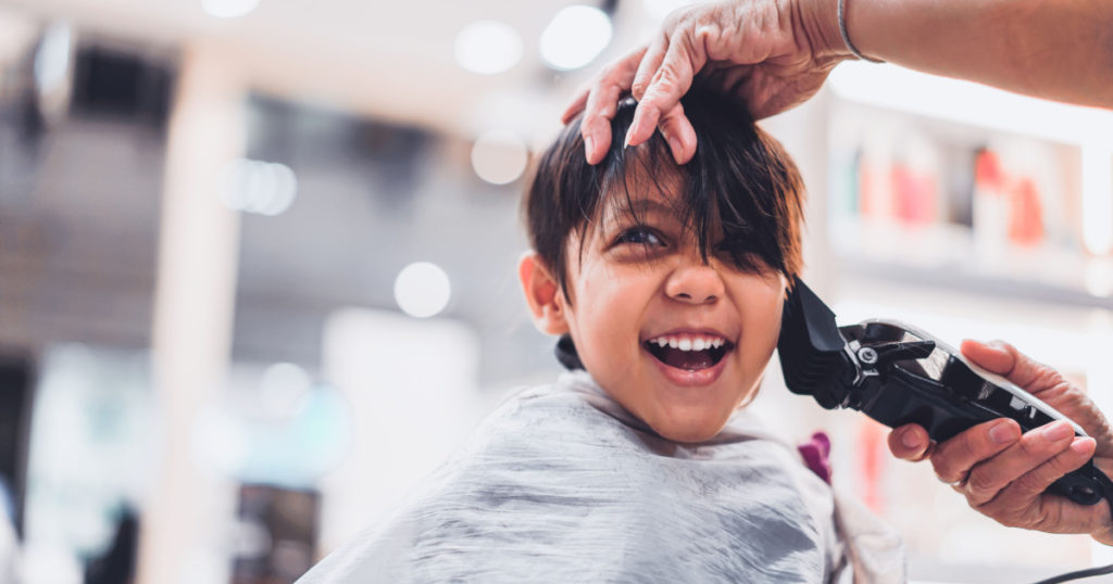 Cute young little boy getting a haircut at salon