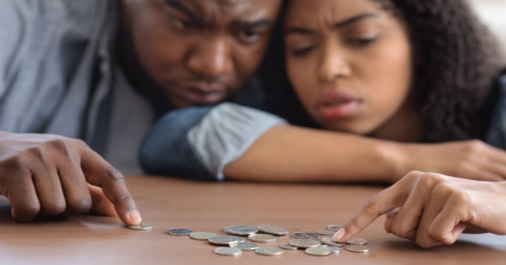 Family Financial Problems. Young Black Couple Counting Remaining Coins On Table, Suffering From Poverty And Absence Of Money, Selective Focus